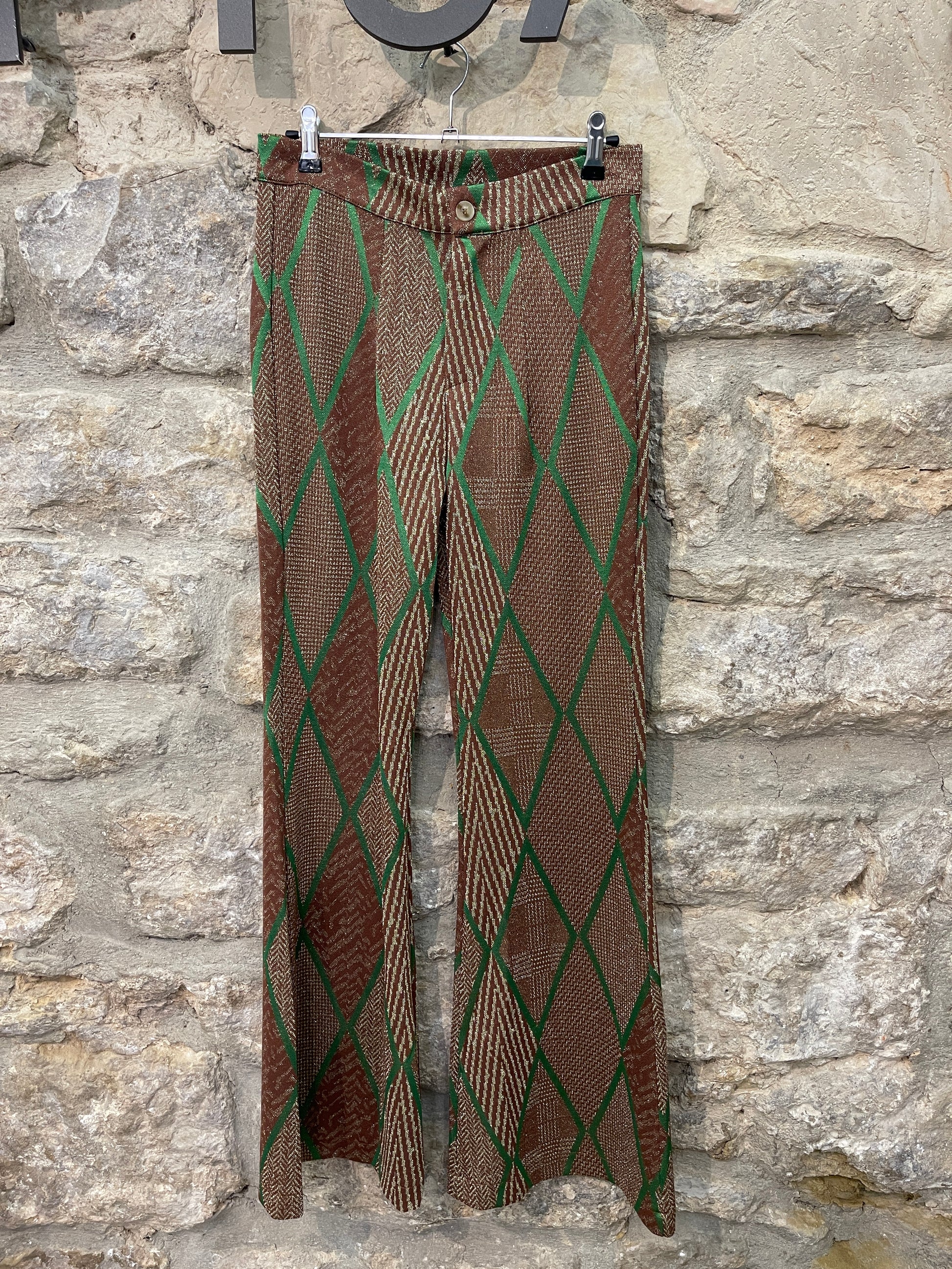 Pantalón de punto en tonos marrones y con estampado a rombos en strass de color verde. Cintura que se cierra con cremallera y botón. Anchos en la parte de abajo.  Composición: 58% Viscosa, 39% Poliéster y 3% Elastano.  Se recomienda lavar a mano o en lavadora hasta 30º. No usar lejía, planchar suavemente del revés hasta 110º y no usar secadora.