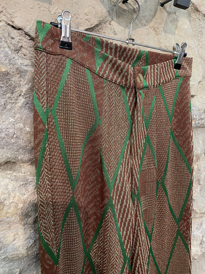 Pantalón de punto en tonos marrones y con estampado a rombos en strass de color verde. Cintura que se cierra con cremallera y botón. Anchos en la parte de abajo.  Composición: 58% Viscosa, 39% Poliéster y 3% Elastano.  Se recomienda lavar a mano o en lavadora hasta 30º. No usar lejía, planchar suavemente del revés hasta 110º y no usar secadora.